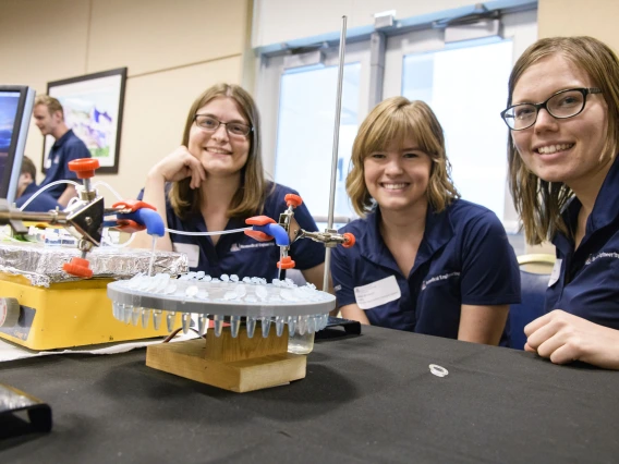 Two senior capstone project members sit next to their pipetting machine