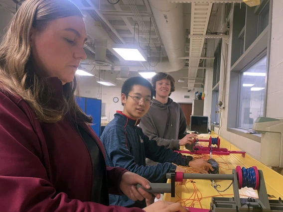 Three students work on a prototype in a machine shop