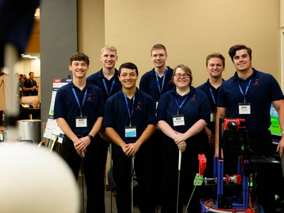 Six men and one women pose for a photo next to a robot with a golf club.