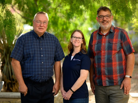 Three employees pose outdoors at the University of Arizona campus