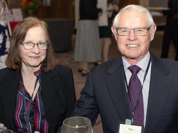 A woman in a striped shirt and a man in a grey blazer smile at the camera.