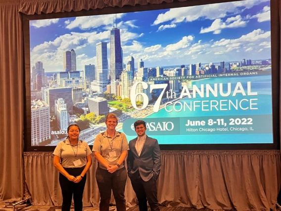 three students stand in front of a conference backdrop