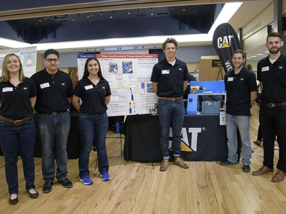 Two women and four men, the members of Team 17010, stand in front of the poster that details their piezoaccelerometer temperature chamber