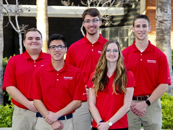 Five university students in red polos standing outside