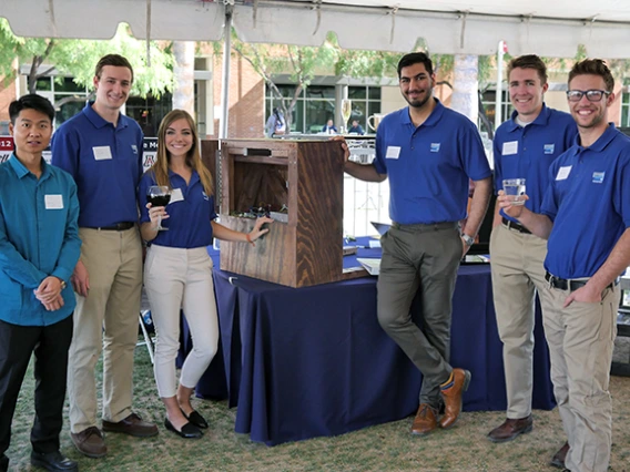 Six university students pose with their turbulence-compensated table mechanism outside under a tent
