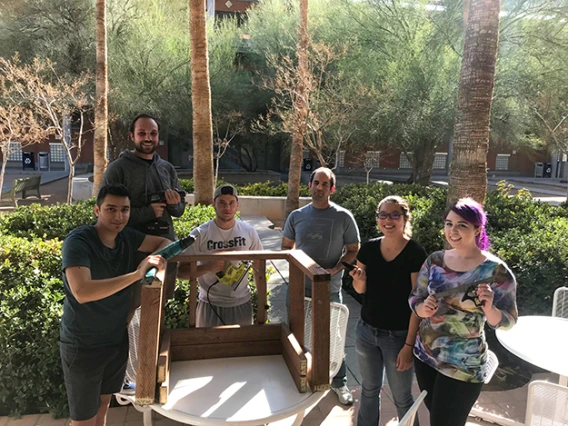 Six university students standing around a wooden structure they are building