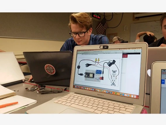 Male student wearing glasses sitting at a laptop with another laptop facing the camera