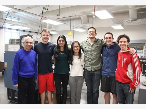 Six university students and an older man standing with their arms around one another in an office