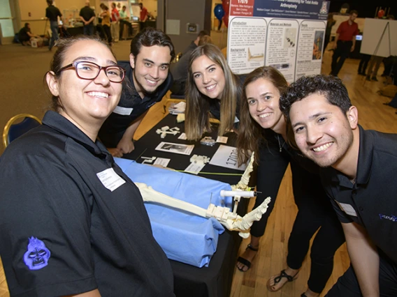 Five students smiling around a skeletal leg model