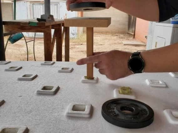 a foam board with square holes in it. a pair of hands is setting a weight on top of a stick that fits into one of the holes.