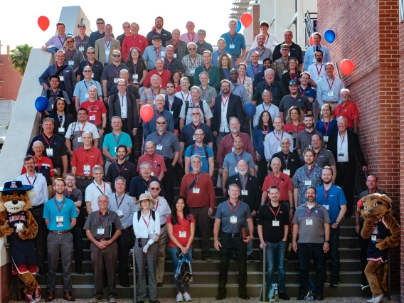 a group of around 100 people stand outdoors on the steps of a building