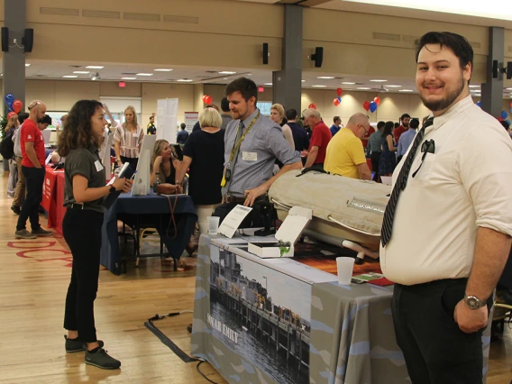 A crowd of smiling sponsors and students stand at dozens of tables in the UA Student Union Ballroom