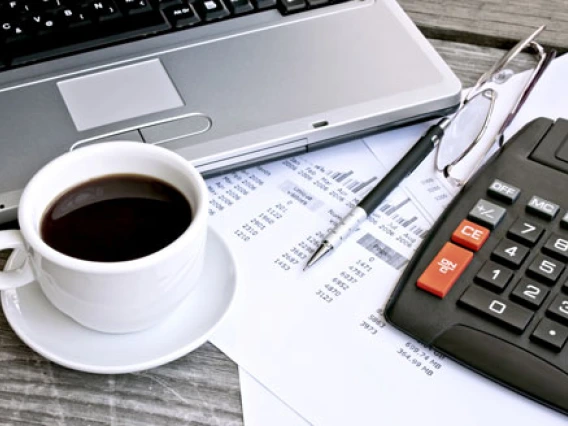 Computer desk with laptop, cup of coffee, and calculator