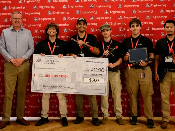 Team members hold a giant check at Design Day.