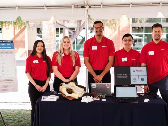 five students standing outside with a conference display