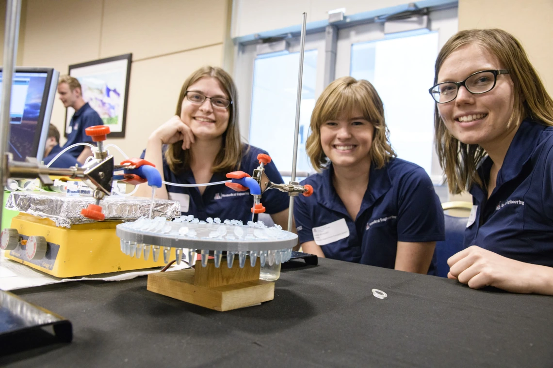 Two senior capstone project members sit next to their pipetting machine