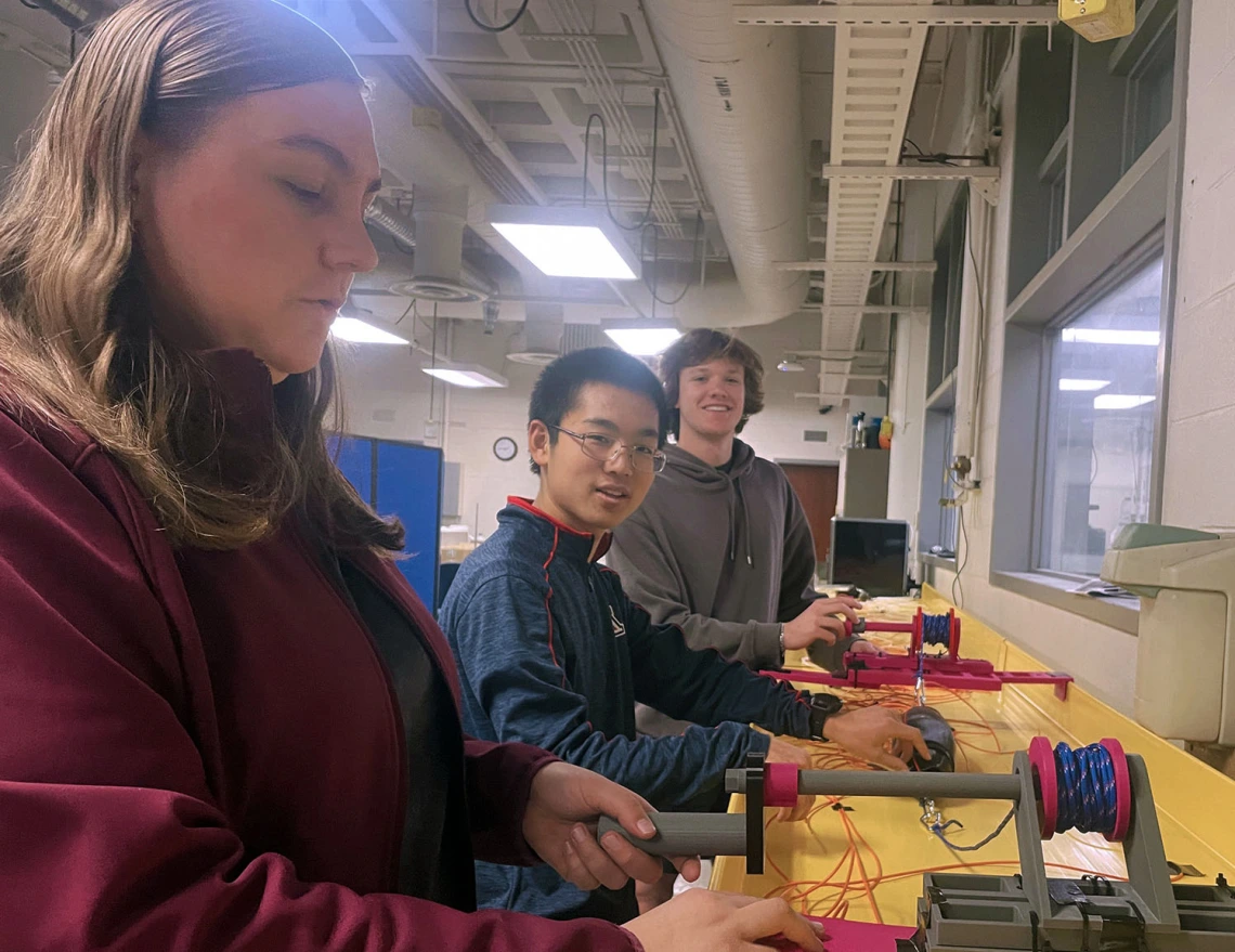 Three students work on a prototype in a machine shop