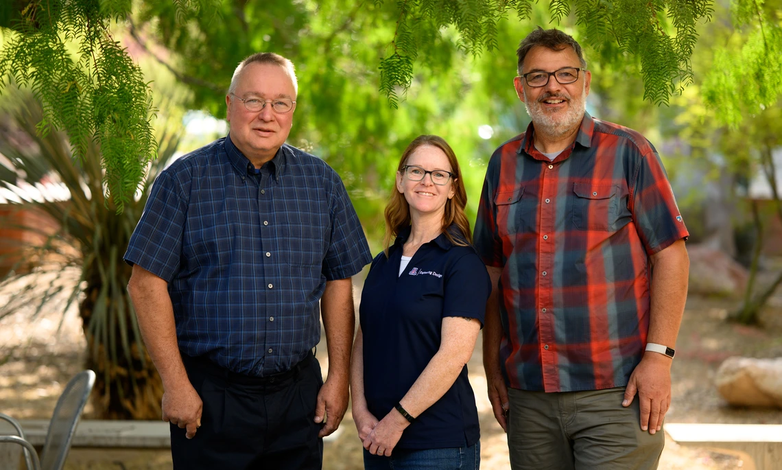 Three employees pose outdoors at the University of Arizona campus