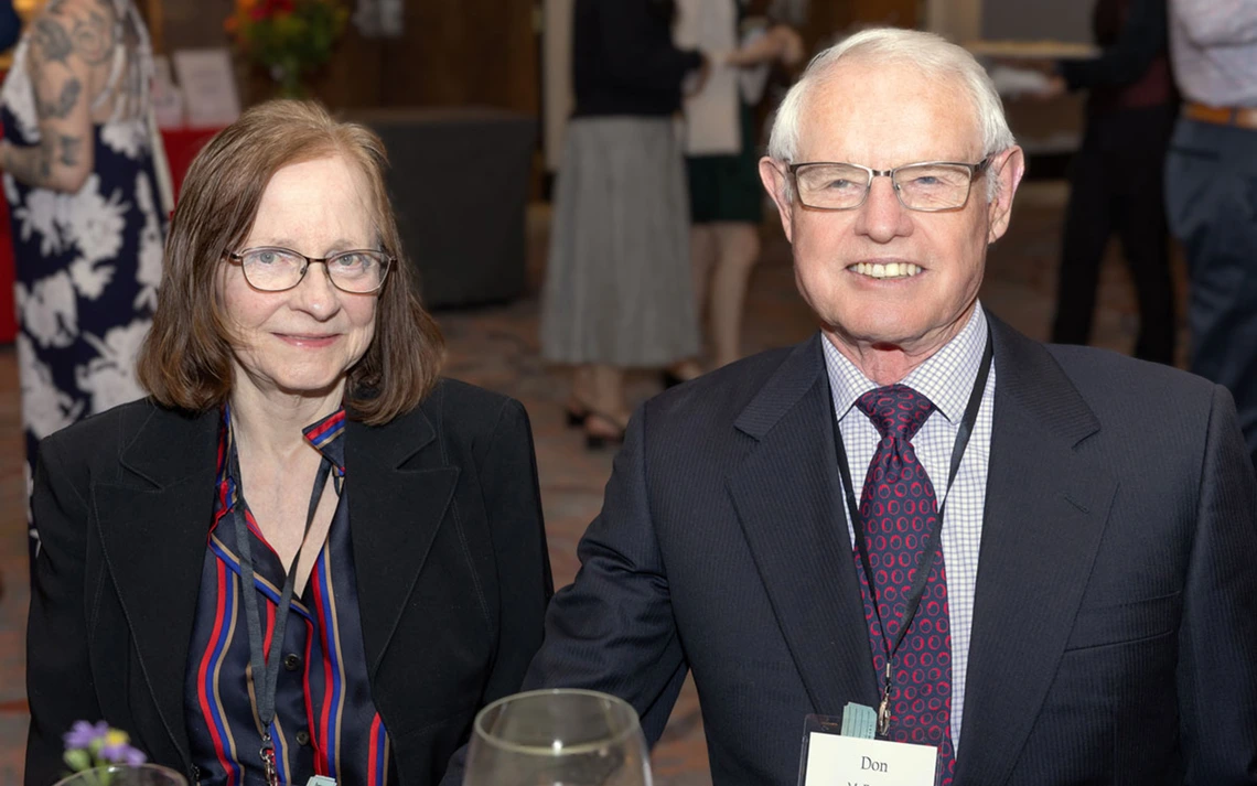 A woman in a striped shirt and a man in a grey blazer smile at the camera.