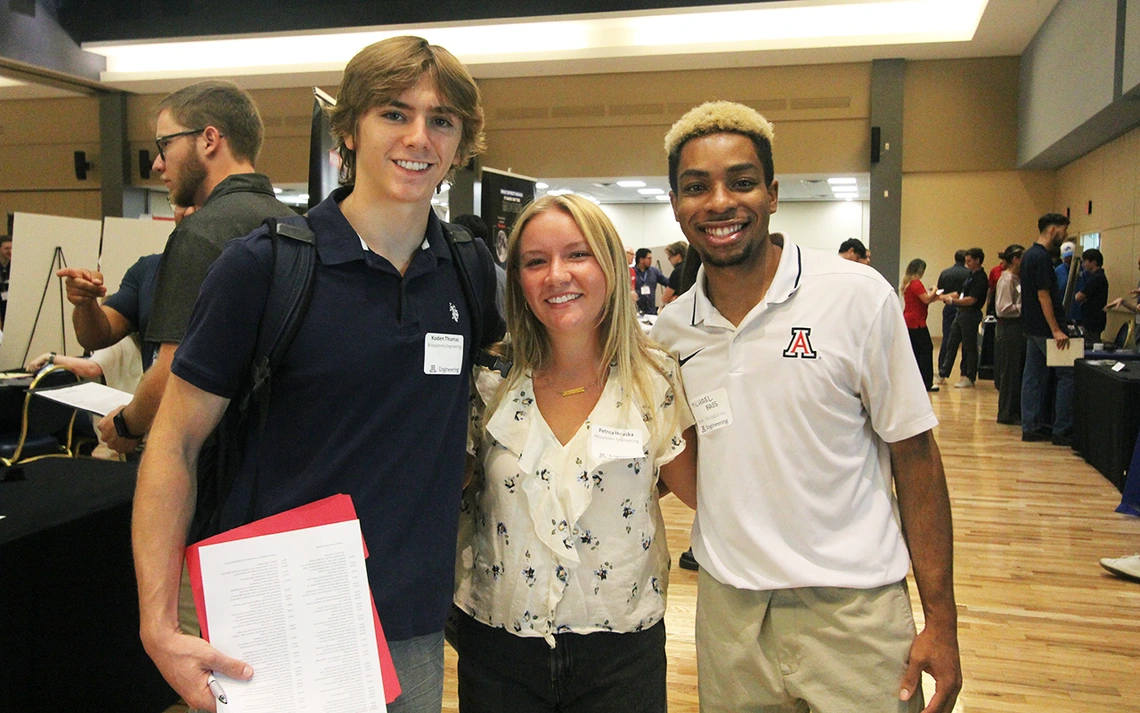 Three students smile for a photo in a large ballroom.