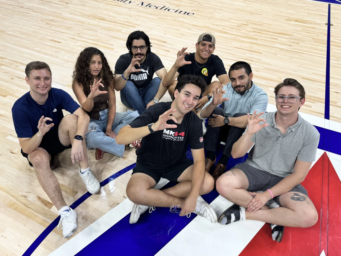 Several students sit on a basketball court.