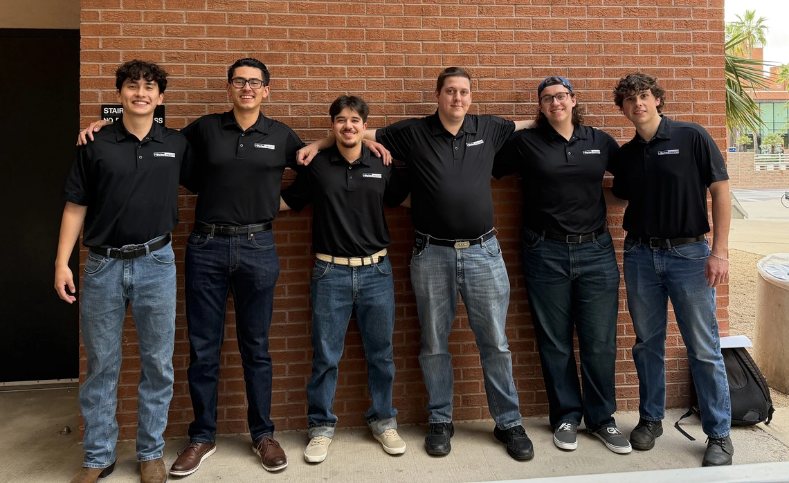 A group of men pose in front of a building.