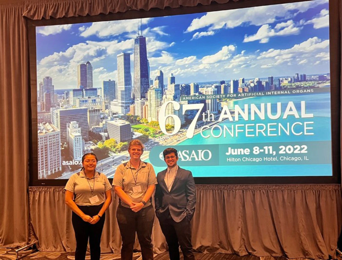 three students stand in front of a conference backdrop