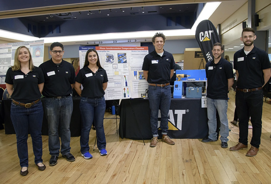 Two women and four men, the members of Team 17010, stand in front of the poster that details their piezoaccelerometer temperature chamber