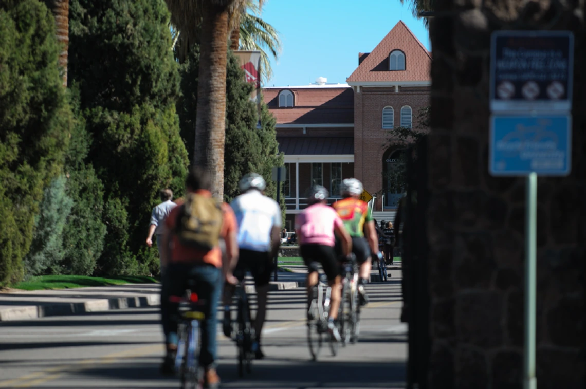 several people ride bicycles on the University of Arizona campus near Old Main