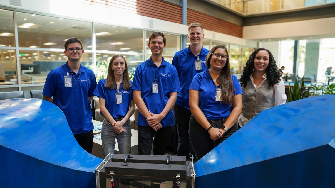 Six people pose behind a subscale wind tunnel