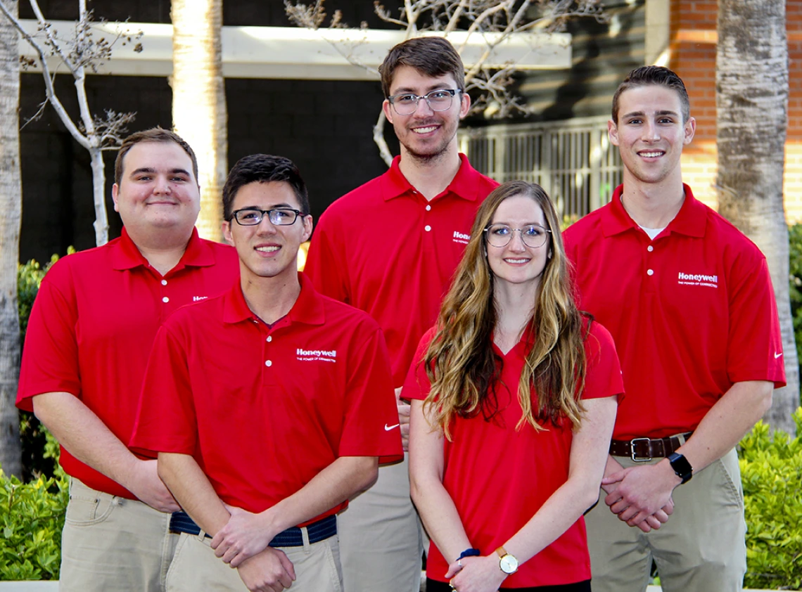 Five university students in red polos standing outside