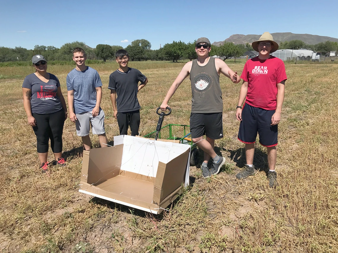 Five people standing in a field with a box attached to a cart