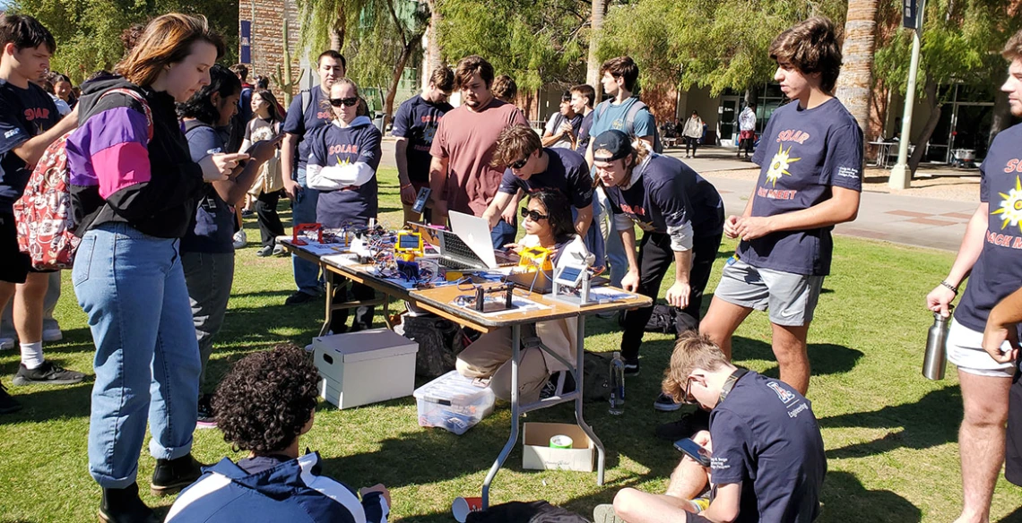 Students gather around a table holding solar trackers