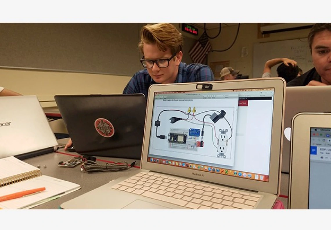 Male student wearing glasses sitting at a laptop with another laptop facing the camera