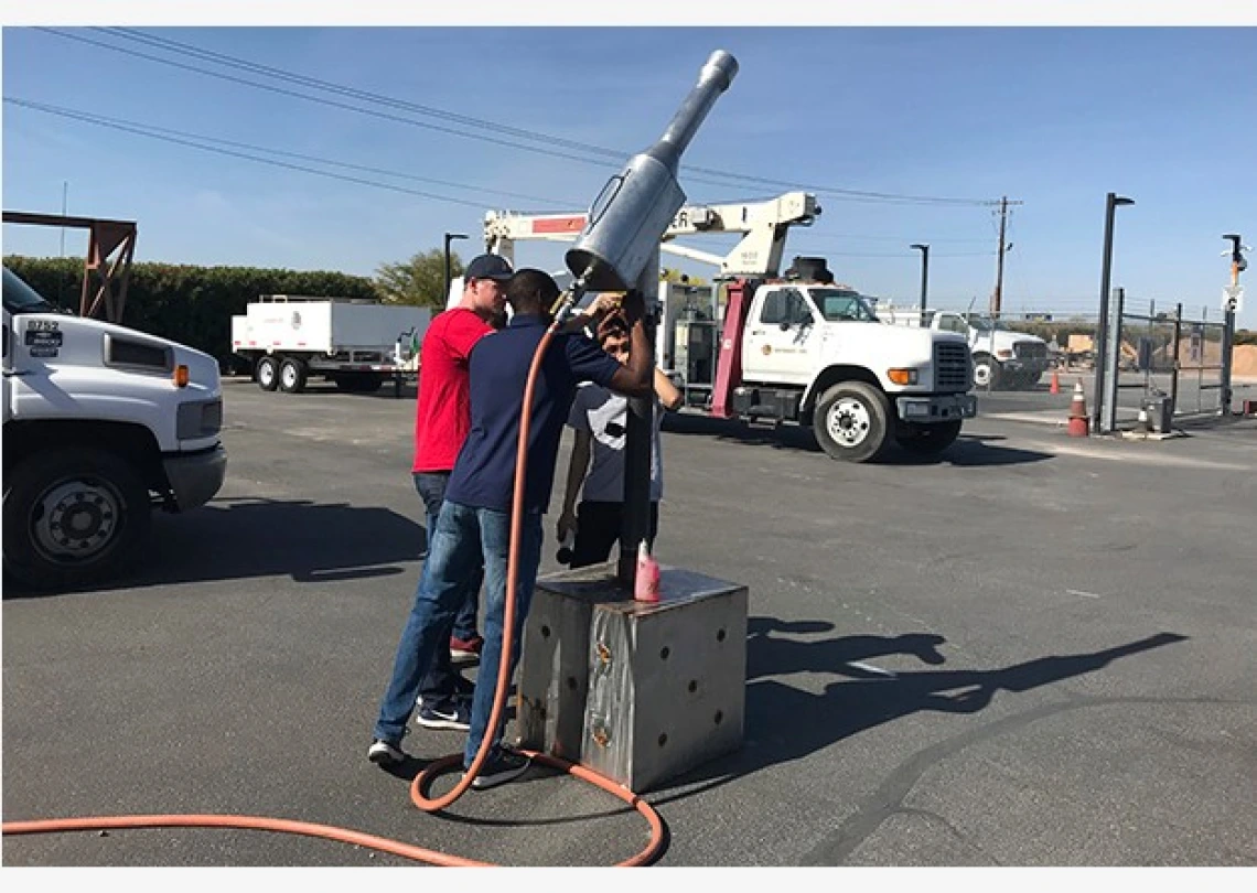 Three university students gathered around a metal contraption for extracting gas