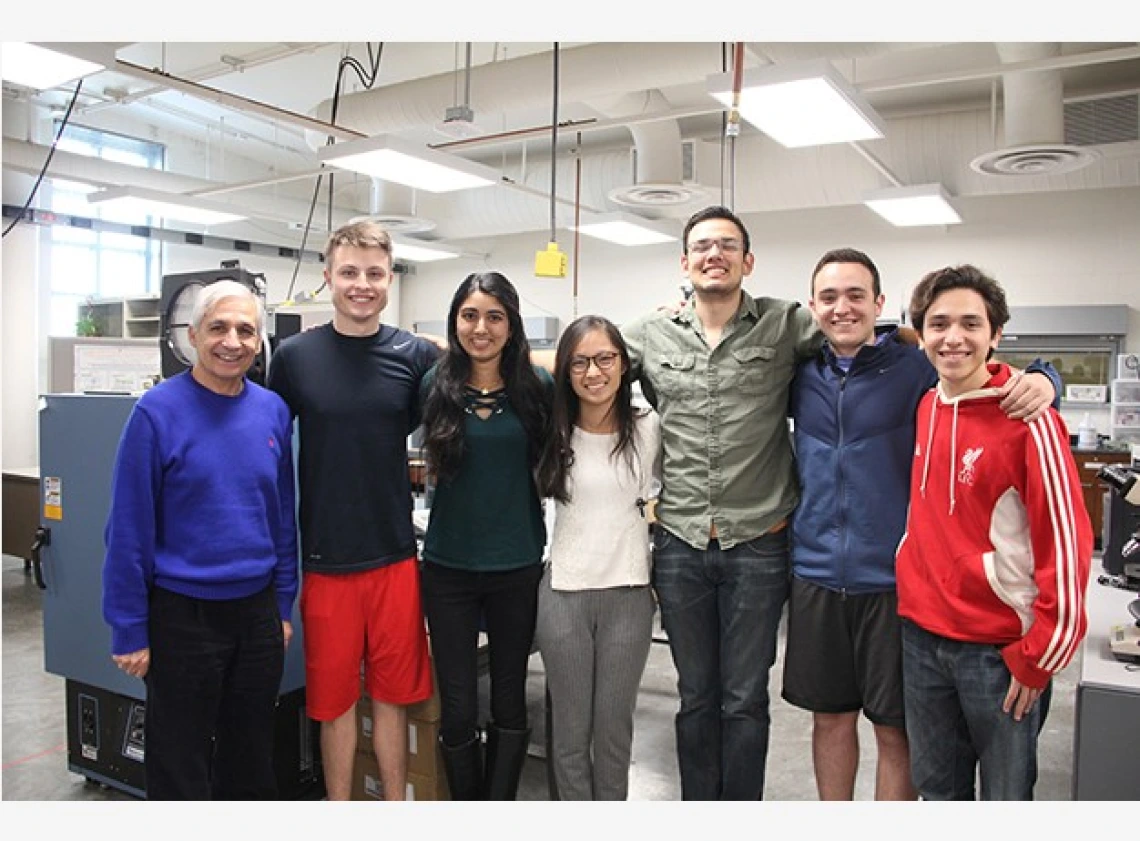 Six university students and an older man standing with their arms around one another in an office