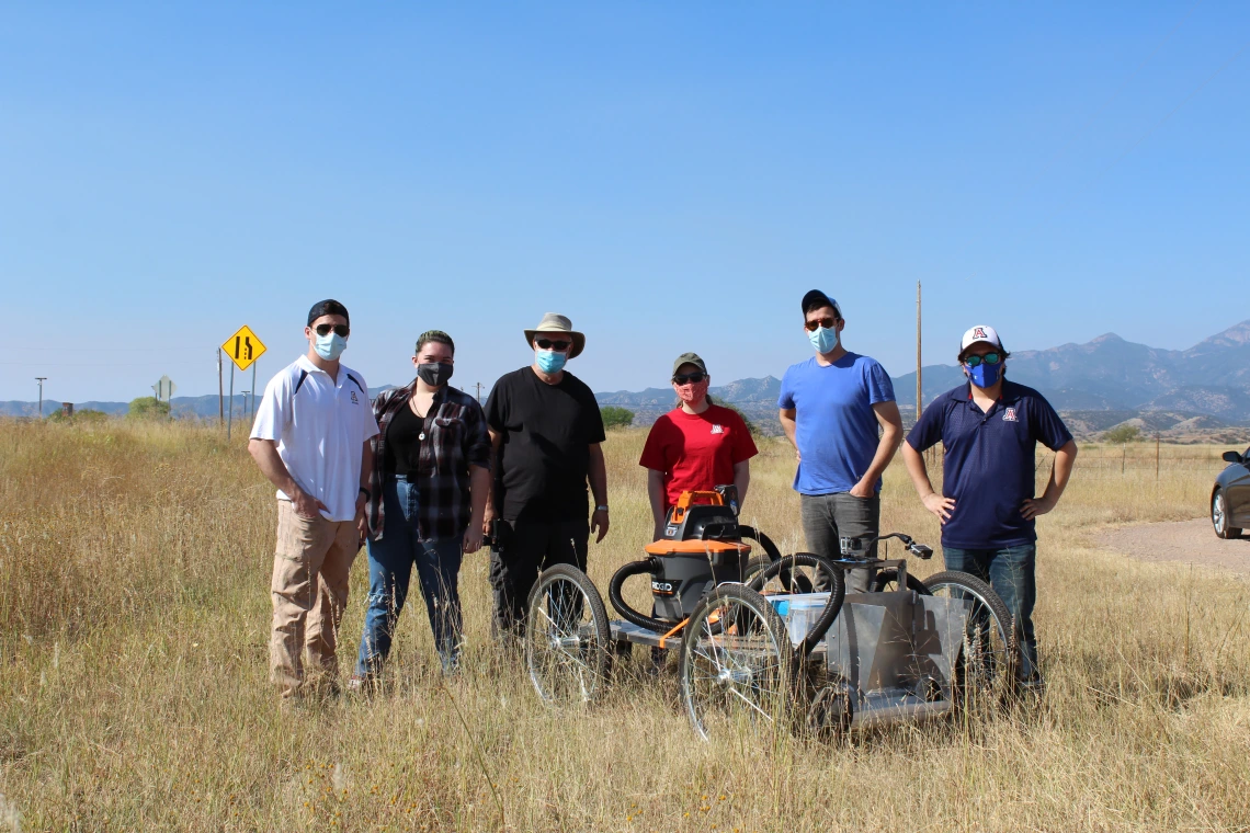 Six people stand in a field around a cart.