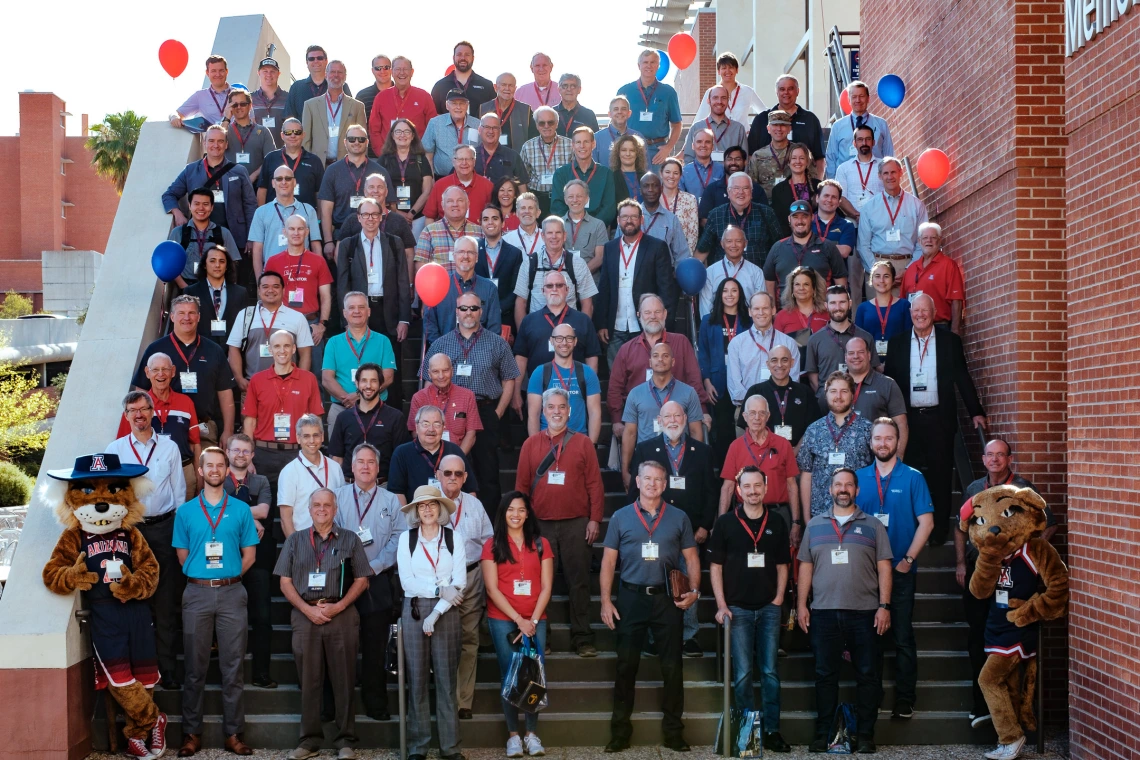 a group of around 100 people stand outdoors on the steps of a building