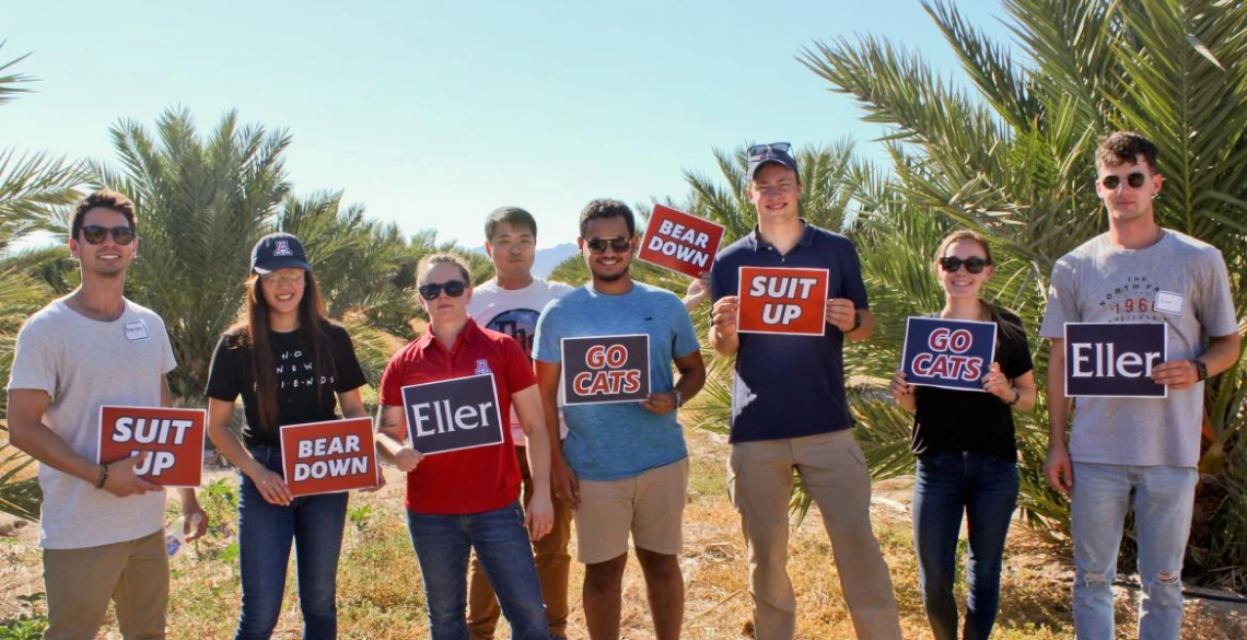 Eight University of Arizona students holding school signs in a date palm field