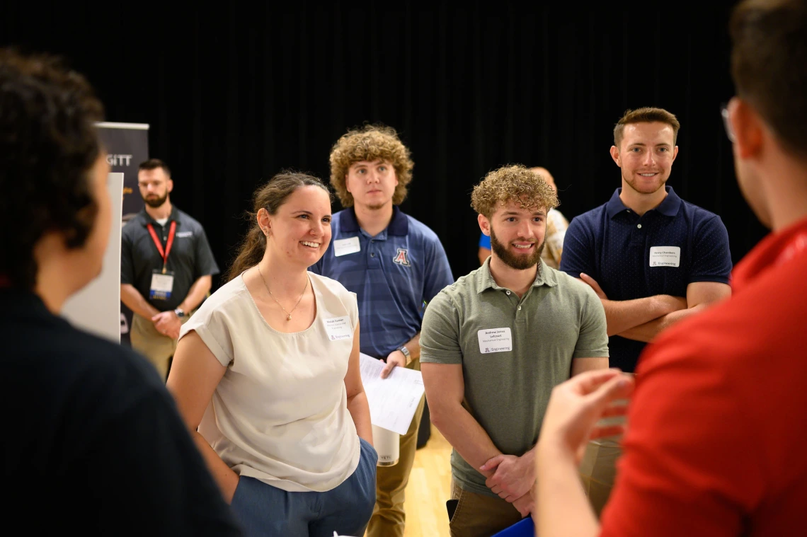 A group of students stands listening to another student speak