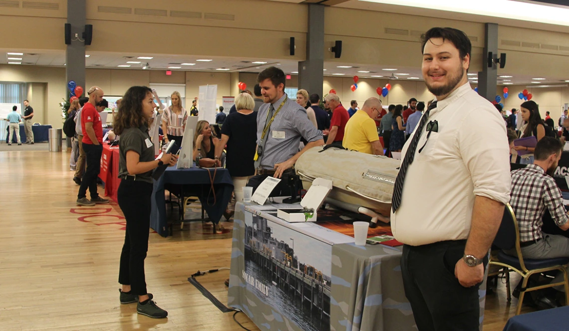 A crowd of smiling sponsors and students stand at dozens of tables in the UA Student Union Ballroom