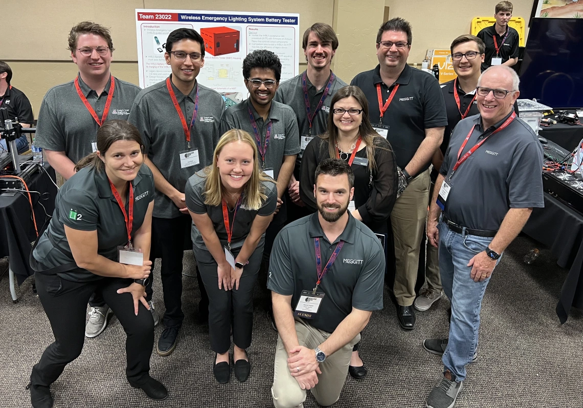 A group of people pose near electronic equipment