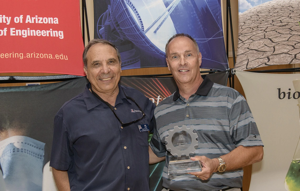 Ron Rich holds his Circle of Excellence Award, a clear trophy in the shape of a gear, while standing next to program director Ara Arabyan.