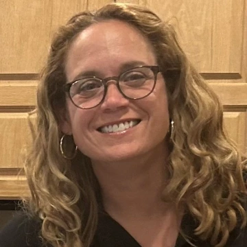 A women with dark blonde hair and silver earrings smiles at the camera.