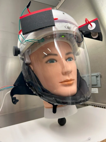 A doll wears a large face shield prototype.