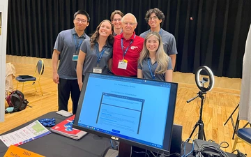 Five students in gray shirts take a photo with an older man.