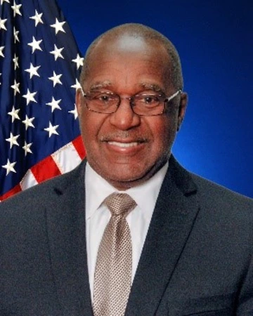 A man in a dark suit takes a photo in front of the American Flag.