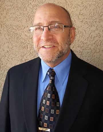 Bob Messenger wearing a suit and tie in front of a brown wall