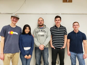 Image of a group of 5 students posing in front of a white wall