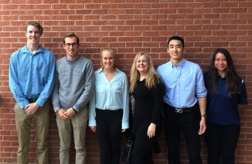 Six people posing in front of a brick wall